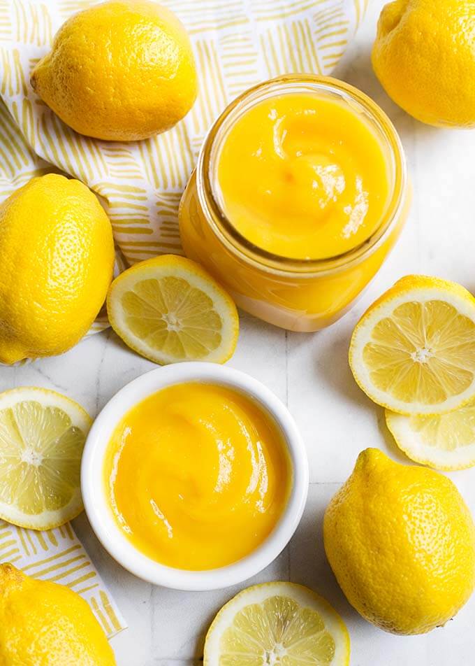 Lemon Curd in a small glass jar and white bowl, all surrounded by cut lemons