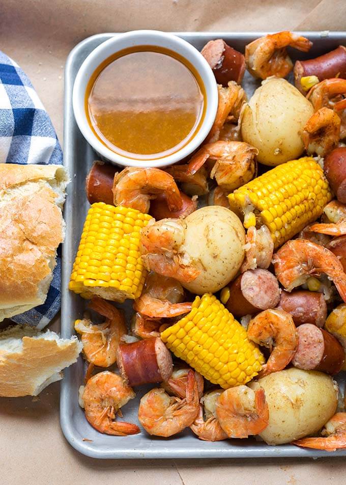 Low Country Shrimp Boil on a baking sheet with small white bowl of brown sauce