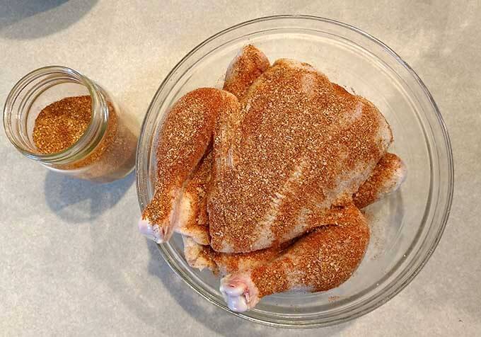 raw whole chicken in a glass mixing bowl with spice rub covering it