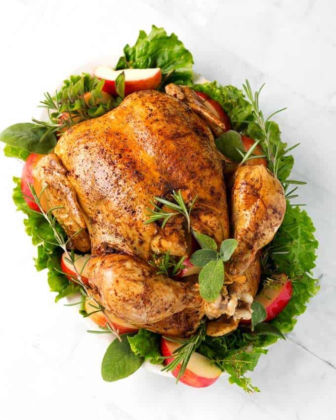 Top view of a cooked Whole Chicken on a white platter with green herbs,leafy vegetables and apple slices