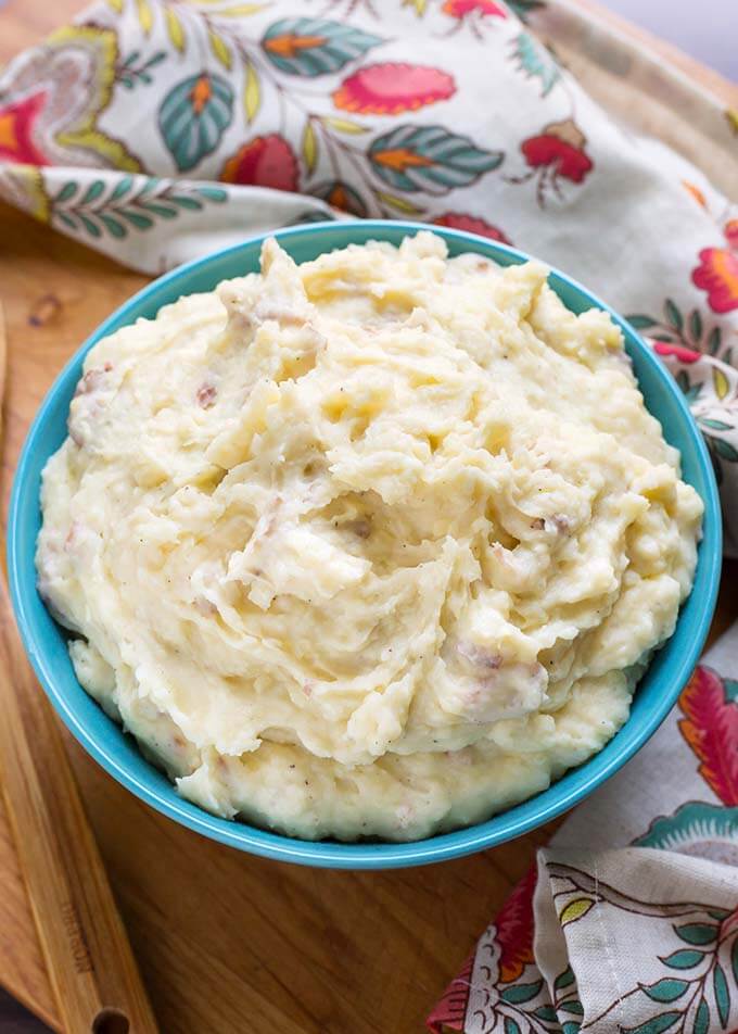 Creamy Mashed Potatoes in a blue bowl and a floral napkin all on a wooden board