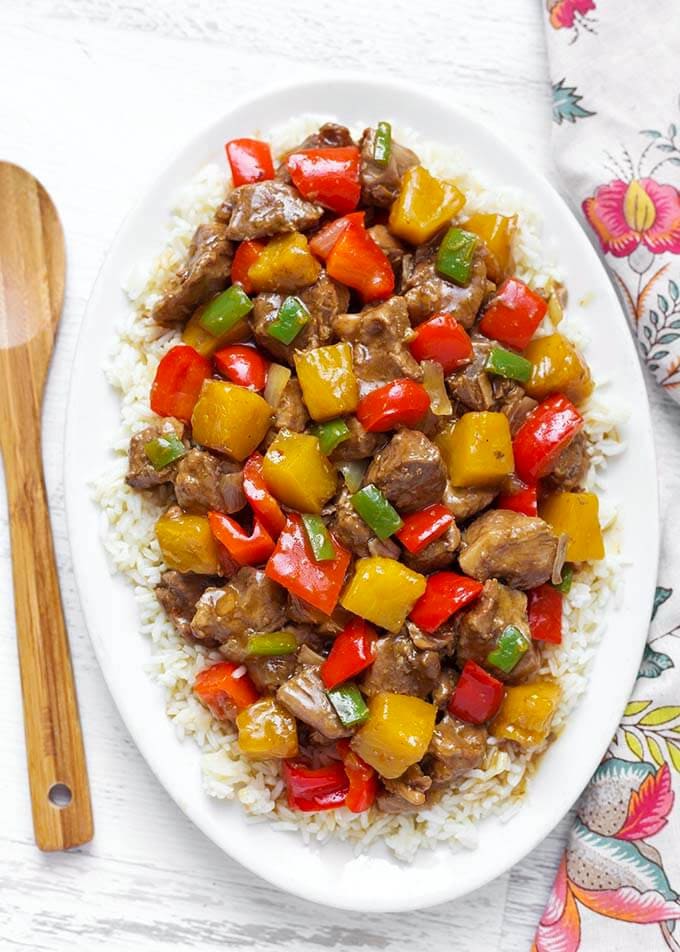 Hawaiian Pineapple Pork over white rice on a white oblong platter next to a wooden mixing spoon