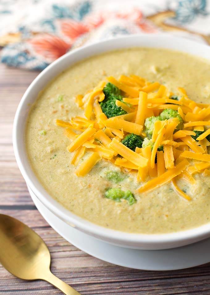 Broccoli Cheddar Soup topped with broccoli and shredded cheese in a white bowl on a white plate