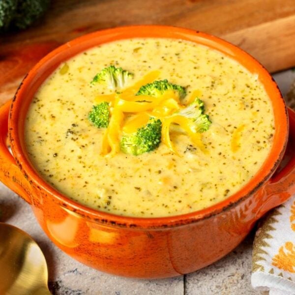 slow cooker broccoli cheddar soup with fresh broccoli and shredded cheddar cheese in an orange bowl