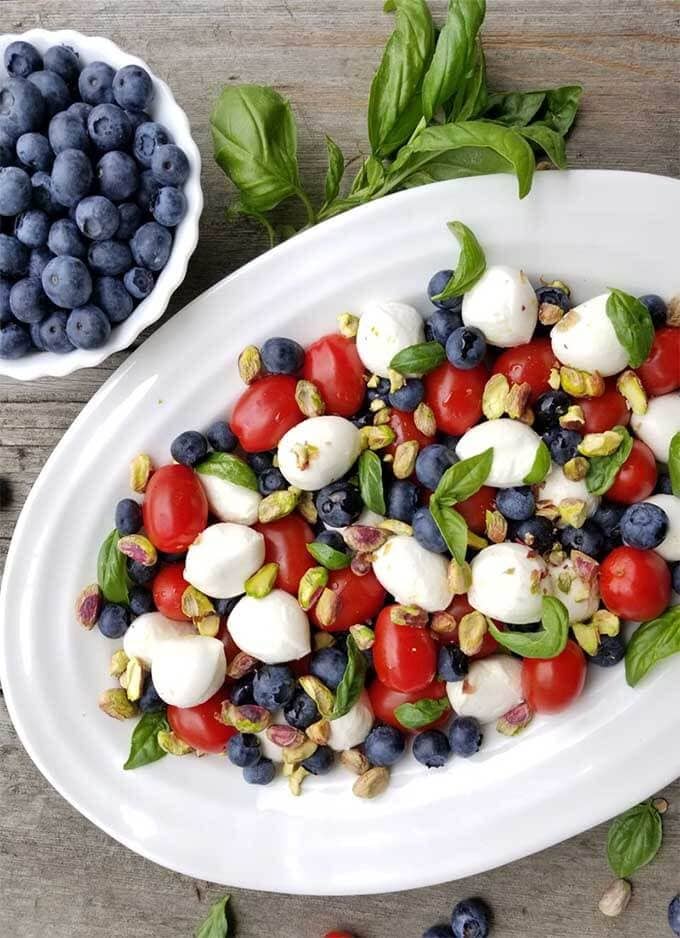 Blueberry Caprese Salad on a white platter next to a bowl of blueberries