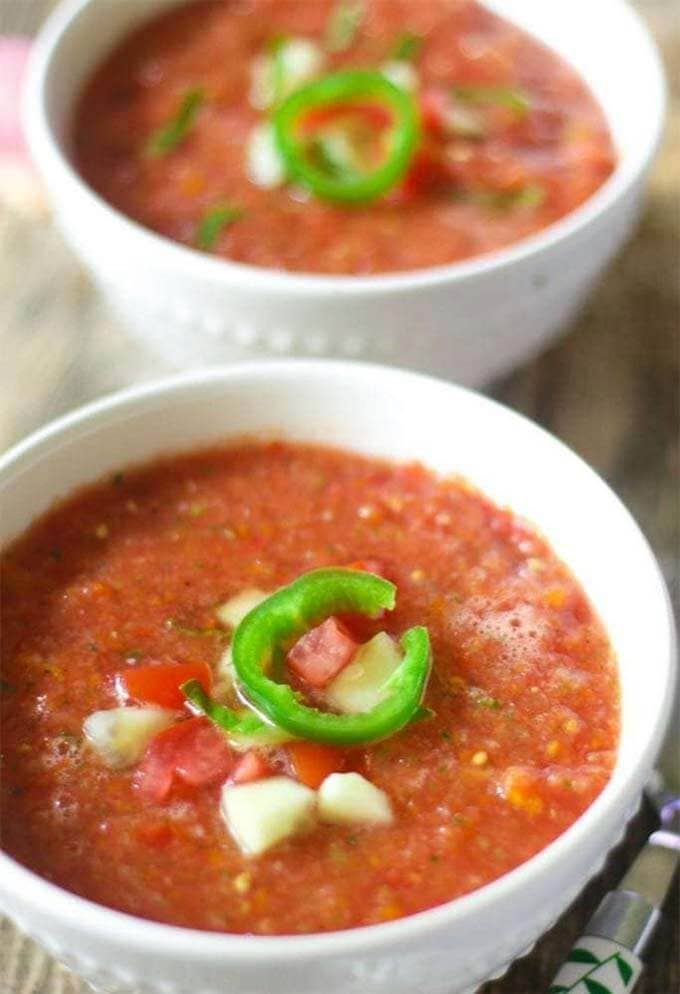 Two white bowls of easy Gazpacho Soup topped with sliced jalapeno