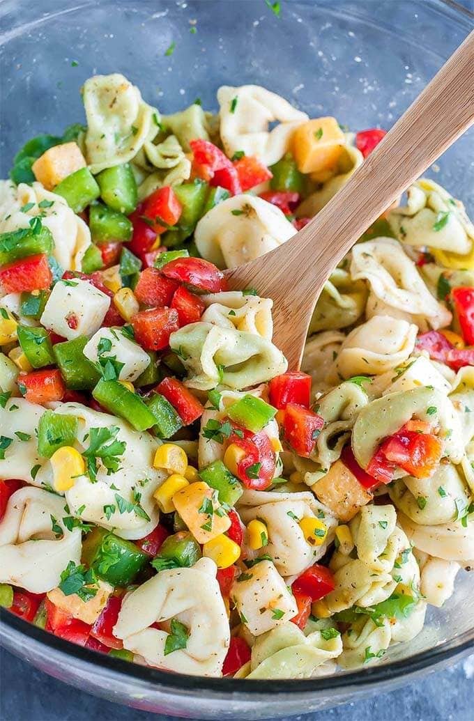 Garden Veggie Tortellini Pasta Salad in a glass bowl with a wooden spoon