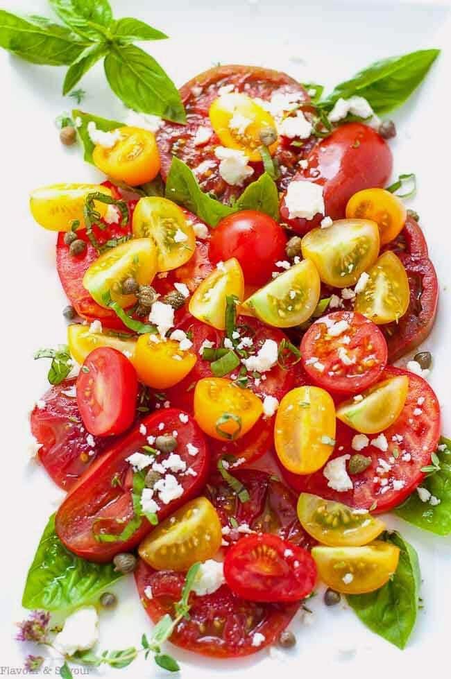 Heirloom Tomato salad with Basil Capers Feta on a white plate