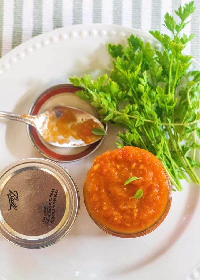 Homemade Basic Tomato Sauce in a small canning jar next to a green herb and canning jar lids