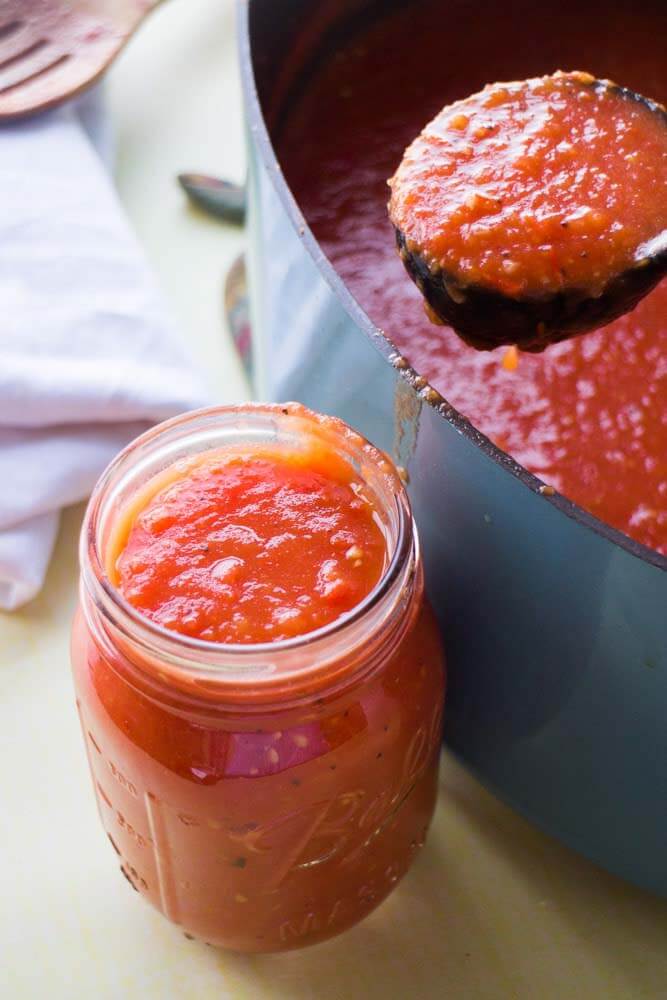 Roma Tomato Sauce in a small canning jar next to a large pot of sauce