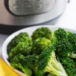 Cooked Broccoli in a white bowl in front of a pressure cooker