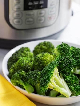 Cooked Broccoli in a white bowl in front of a pressure cooker