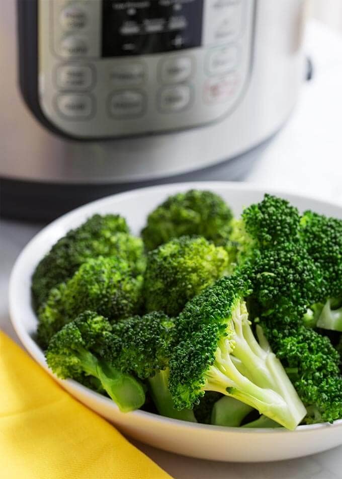 Cooked Broccoli in a white bowl in front of a pressure cooker