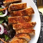 sliced chicken breast on a white plate next to a salad