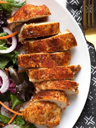 sliced chicken breast on a white plate next to a salad