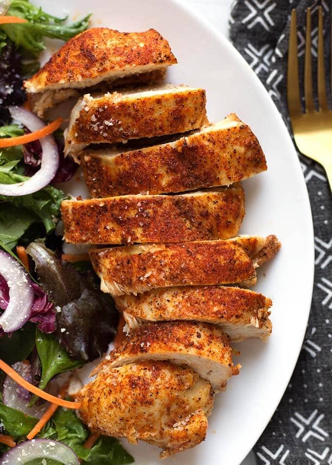 sliced chicken breast on a white plate next to a salad