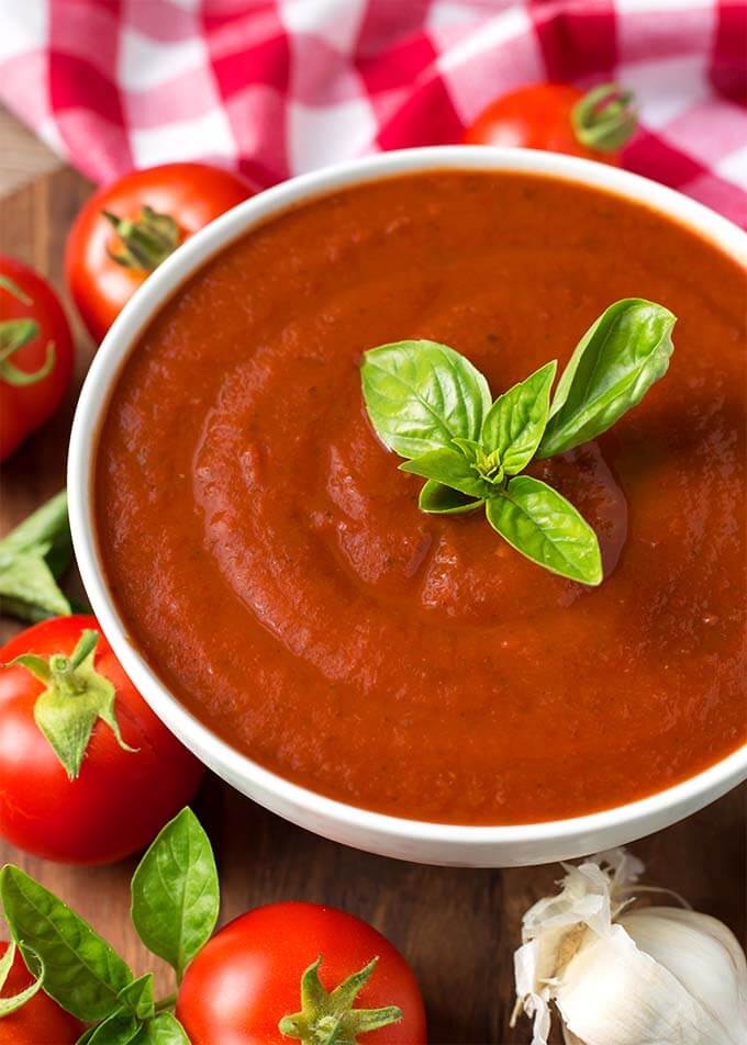 Marinara Fresh Tomato Sauce in a white bowl topped with fresh basil surrounded by ingredients and a red gingham napkin