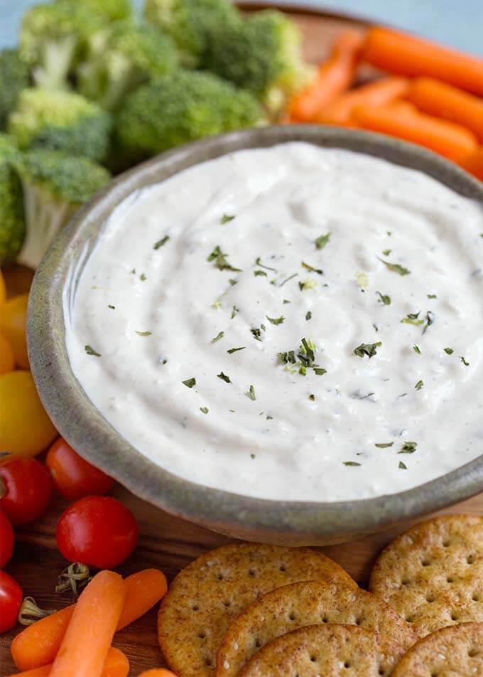 Closeup of Ranch Vegetable Dip in a gray bowl on a round wooden board surrounded by vegetables and crackers