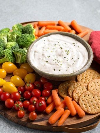 Ranch Vegetable Dip in a gray bowl on a round wooden board surrounded by vegetables and crackers