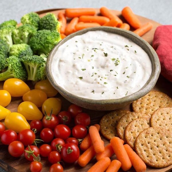 Ranch Vegetable Dip in a gray bowl on a round wooden board surrounded by vegetables and crackers