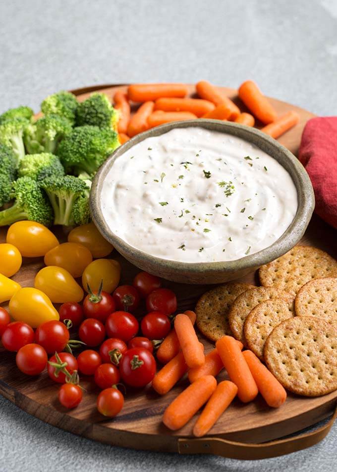 Ranch Vegetable Dip in a gray bowl on a round wooden board surrounded by vegetables and crackers