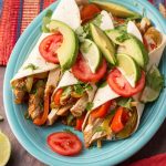 Three Chicken Fajitas topped with sliced avocado and tomatoes a blue plate