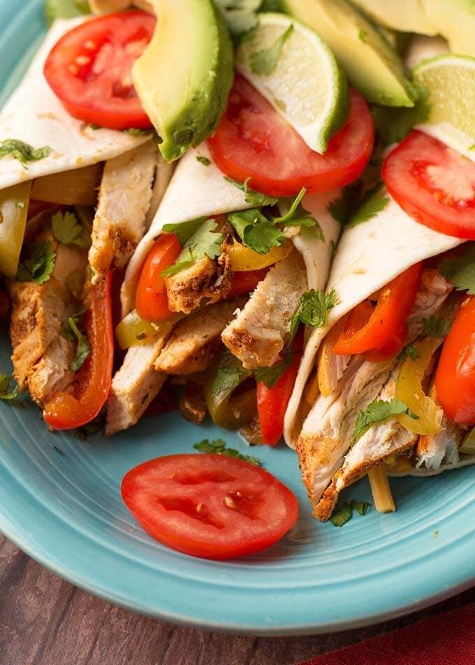 Closeup of three Chicken Fajitas topped with sliced avocado and tomatoes on a blue plate