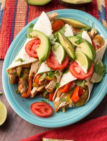 Three Chicken Fajitas topped with sliced avocado and tomatoes a blue plate