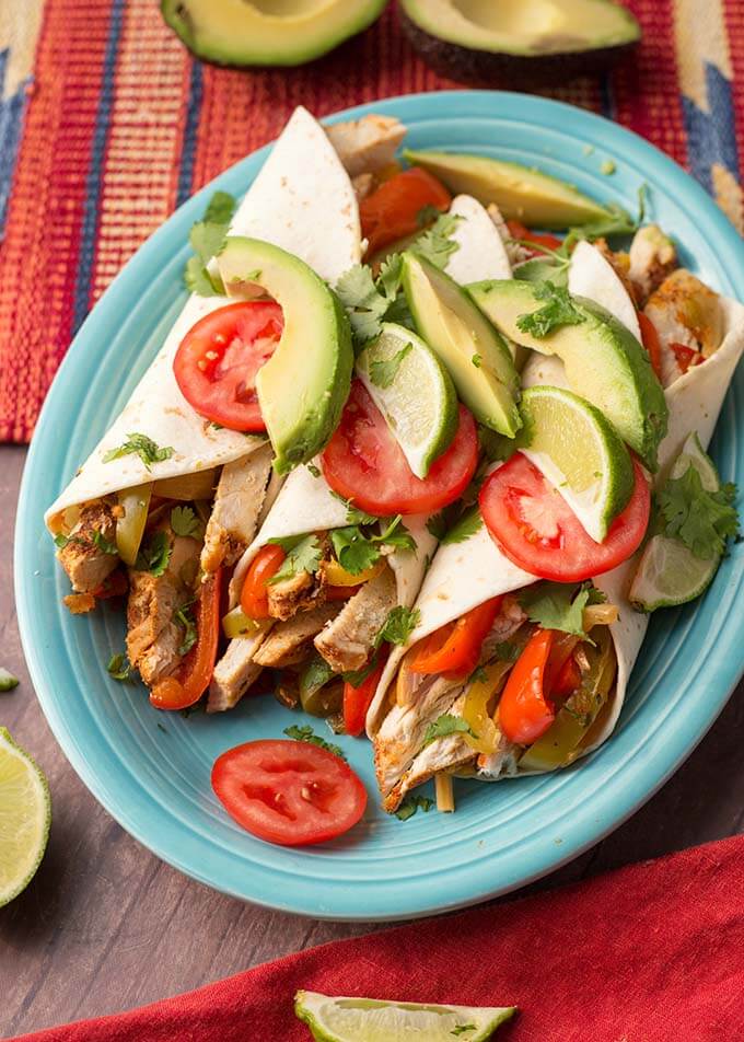 Three Chicken Fajitas topped with sliced avocado and tomatoes a blue plate
