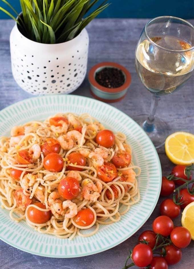 Tomato, garlic, and prawn spaghetti on a white and turquoise plate next to cherry tomatoes and potted plant