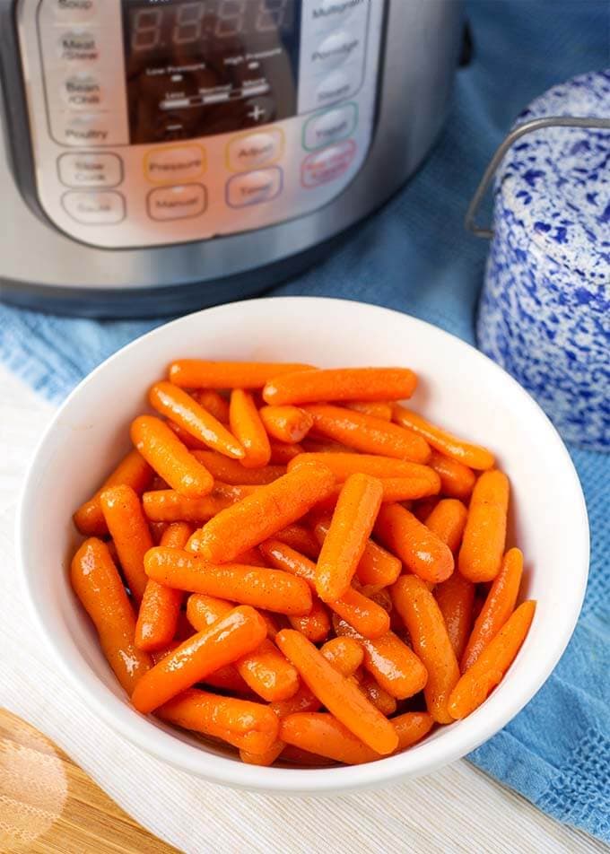 Cinnamon Glazed Carrots in a white bowl in front of a pressure cooker
