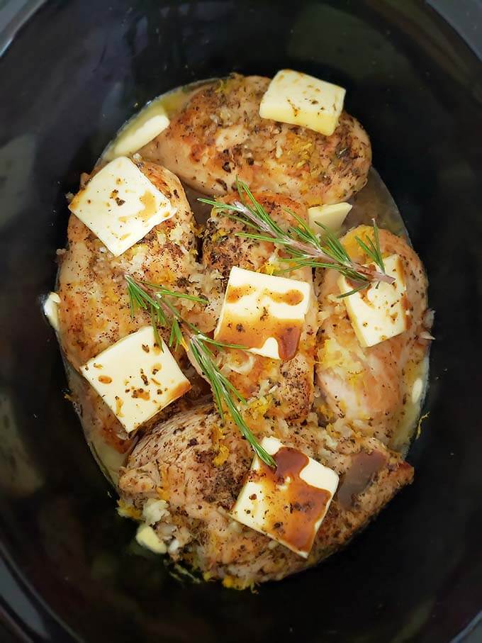 Creamy Lemon Chicken Breasts with slices of butter and fresh rosemary in a slow cooker
