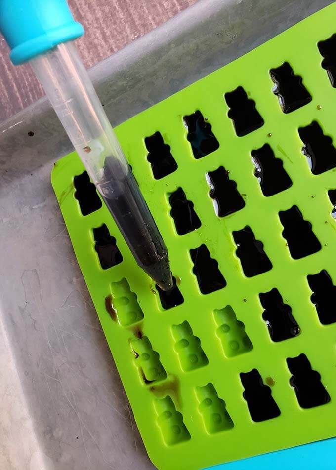 Dropper full of Elderberry gummy mixture filling in bear shaped cavities of a silicon mold