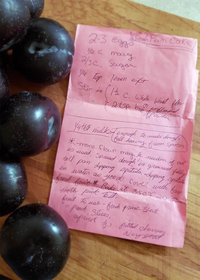 Several fresh plums and pink paper with recipe on a wooden board