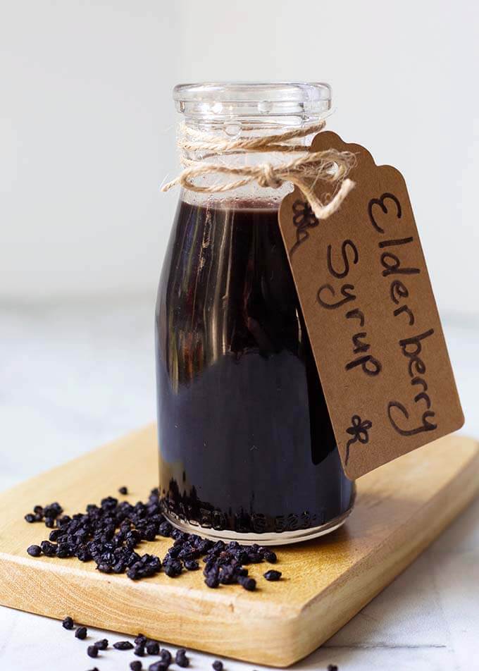 Small bottle of Elderberry Syrup with tap tied with twine on a wooden board with dried elderberries