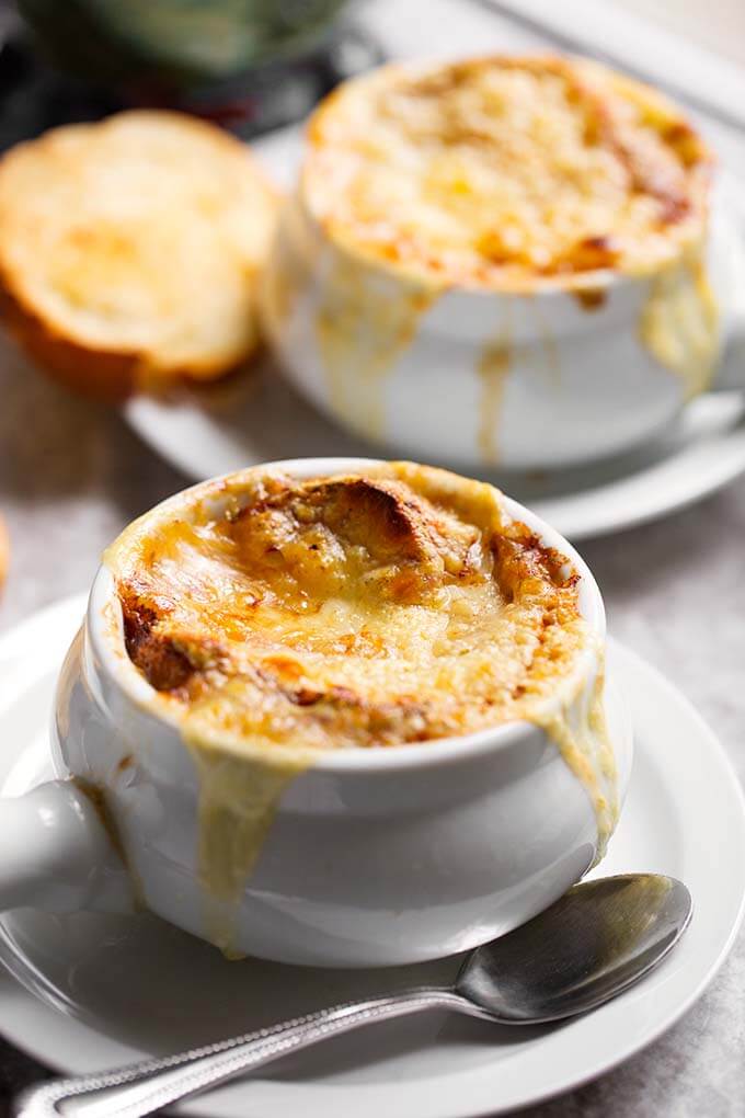 French Onion Soup with melted cheese and small slice of toasted bread on white plates