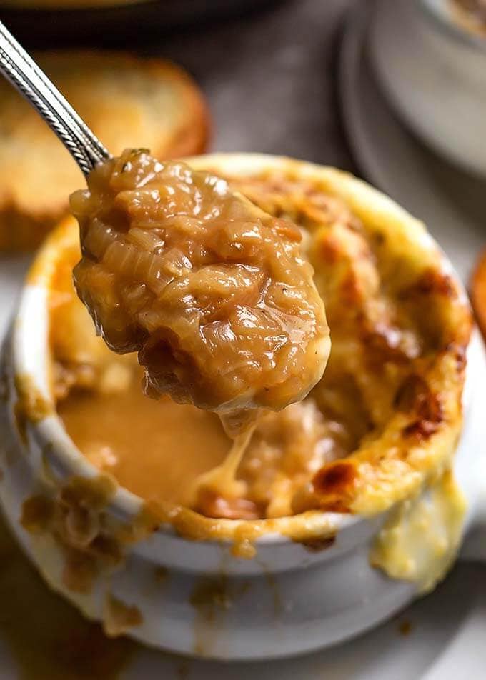 Closeup of a spoonful of French Onion Soup over bowl of remaining soup