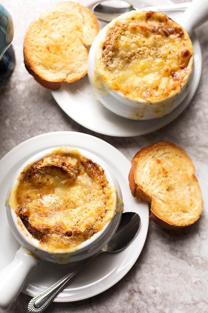 Top view of two bowls of French Onion Soup with melted cheese and small slice of toasted bread on white plates