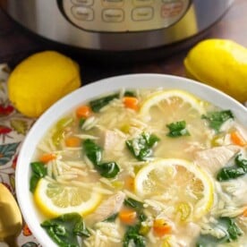Lemon Chicken Orzo Soup in a white bowl in front of a pressure cooker is a light and delicious soup that you can make in minutes. This pressure cooker lemon chicken orzo soup is a healthy and simple Instant Pot chicken soup. simplyhappyfoodie.com #instantpotchickensoup #instantpotsoup #pressurecookerchickensoup