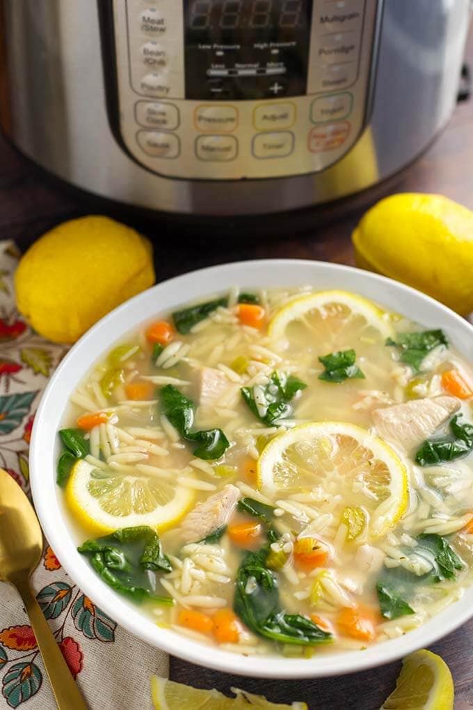 Lemon Chicken Orzo Soup in a white bowl in front of a pressure cooker is a light and delicious soup that you can make in minutes. This pressure cooker lemon chicken orzo soup is a healthy and simple Instant Pot chicken soup. simplyhappyfoodie.com #instantpotchickensoup #instantpotsoup #pressurecookerchickensoup