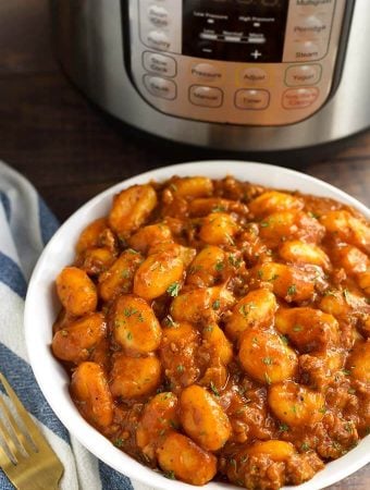 Sausage Gnocchi in a white bowl in front of a pressure cooker