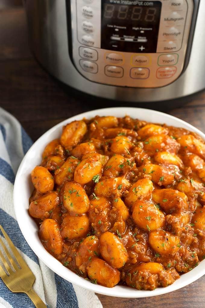Sausage Gnocchi in a white bowl in front of a pressure cooker