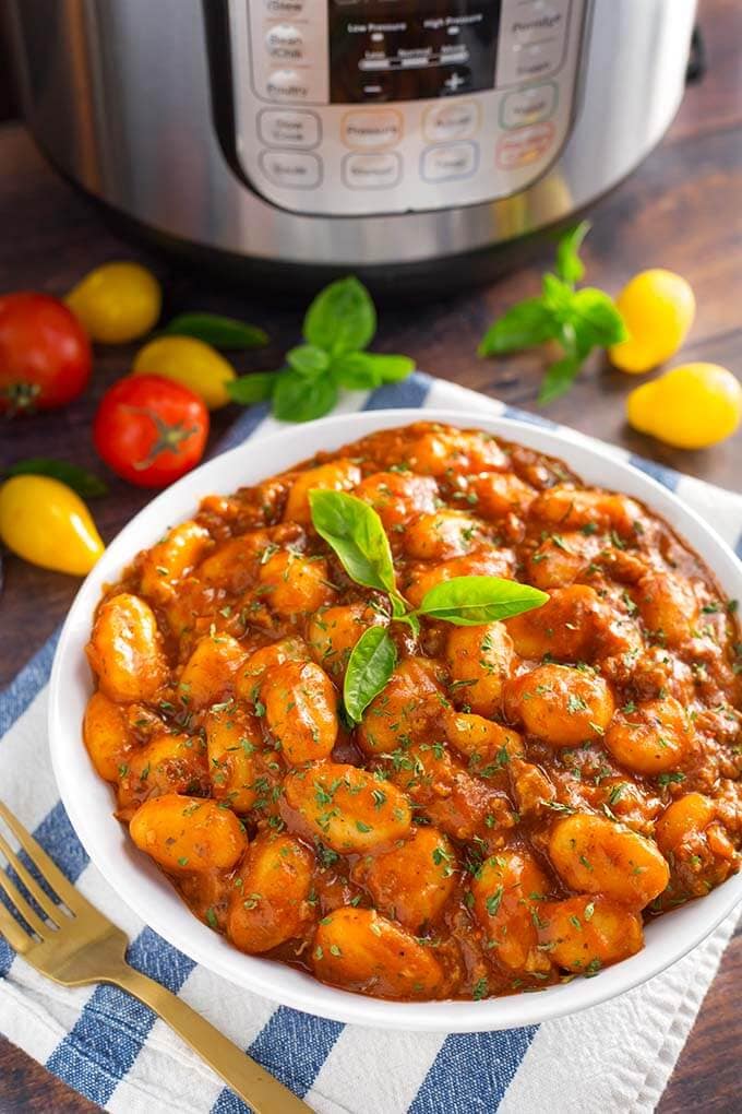 Sausage Gnocchi topped with fresh basil in a white bowl on a blue and white stripped napkin in front of a pressure cooker