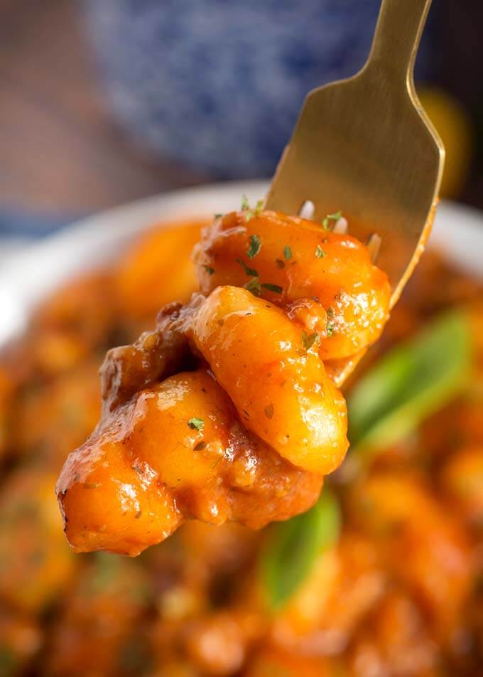 Closeup of a fork holding Sausage Gnocchi over white bowl of Sausage Gnocchi