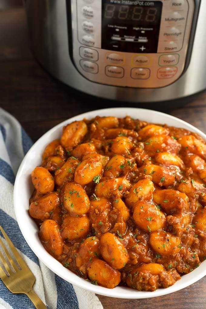 White bowl of Sausage Gnocchi in front of a pressure cooker