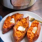 Three cooked sweet potatoes with butter and a fork on a white plate in front of a pressure cooker