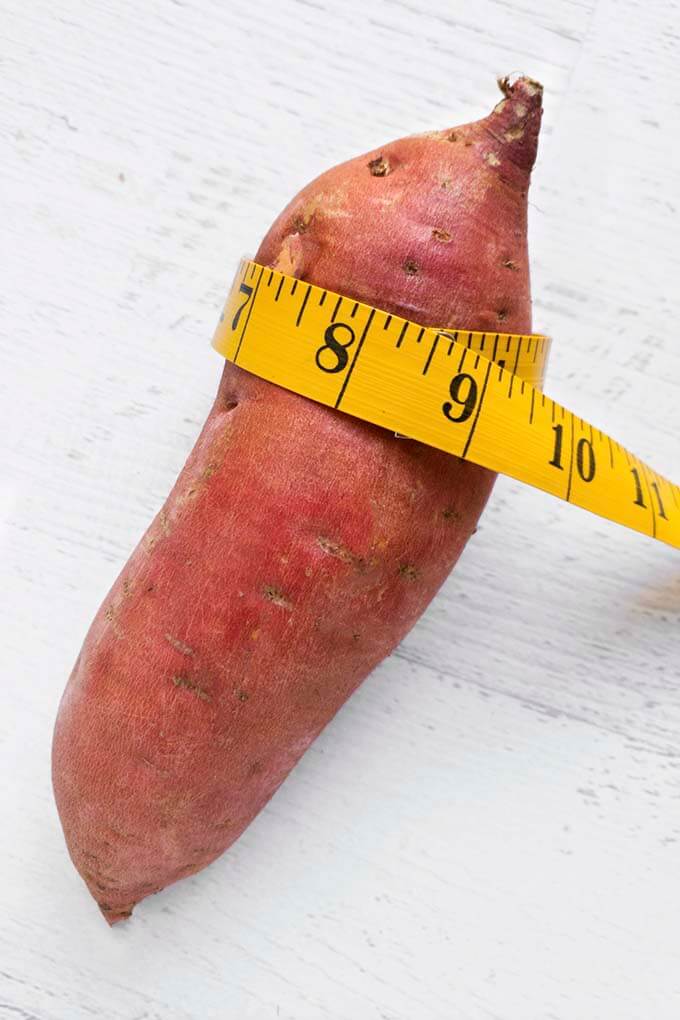 Yellow measuring tape measuring raw sweet potato
