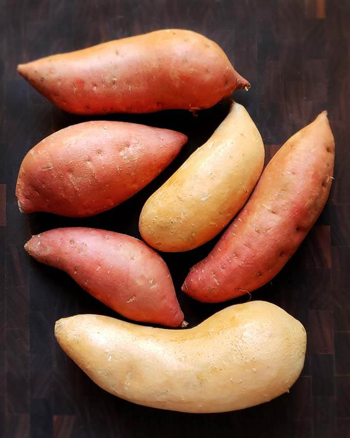 Six uncooked sweet potatoes on a dark wooden surface