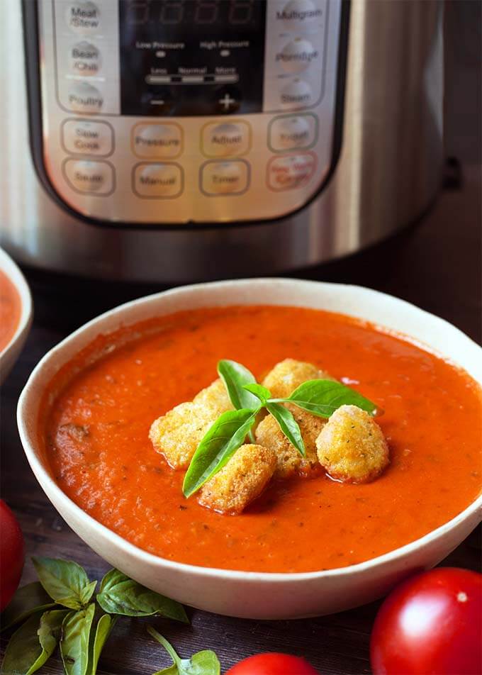 Fresh Tomato Basil Soup topped with croutons and fresh basil in a white bowl in front of a pressure cooker