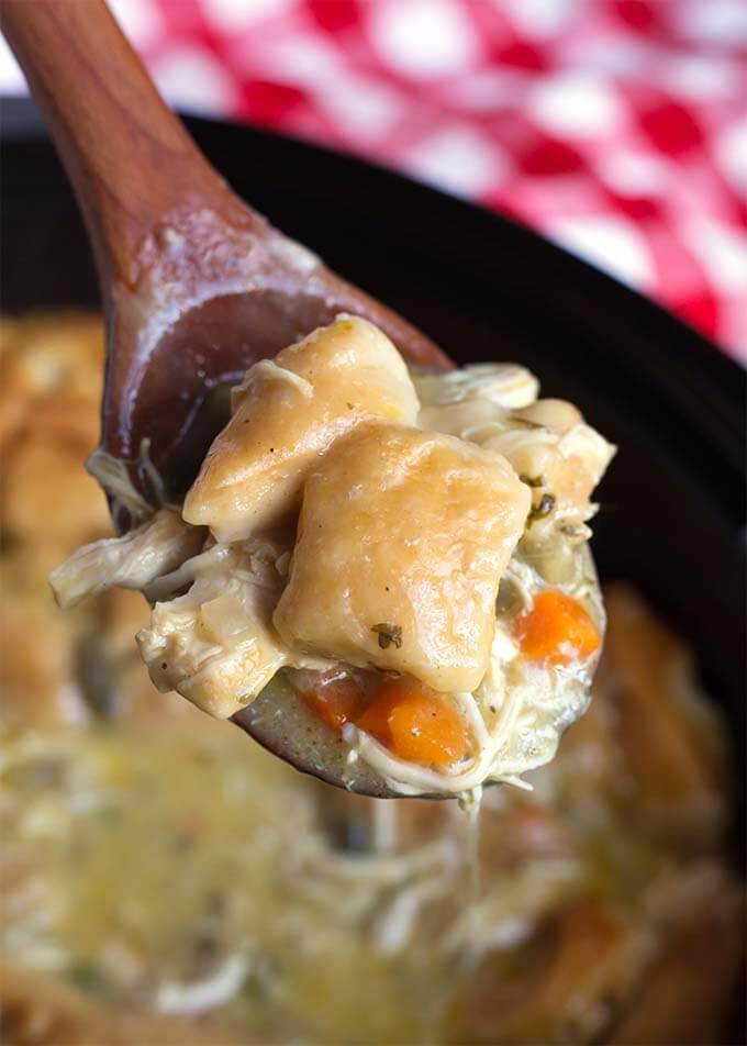 Closeup of a wooden spoon full of Chicken and Dumplings over the slow cooker